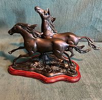 Full view of two-horse cast metal sculpture on red wood base
