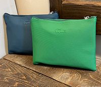 Front view of green and blue Lacoste zip pouches