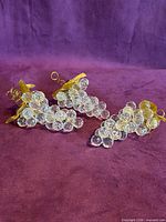 Three clear lucite grape clusters with gold-tone leaves on purple backdrop
