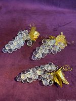 Three clear lucite grape clusters with gold leaves on purple backdrop