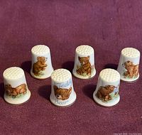Six ceramic teddy bear thimbles upright on fabric background