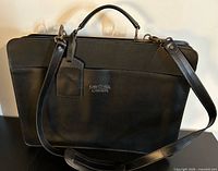 Front view showing leather briefcase with handles, shoulder strap, tag, embossed logo