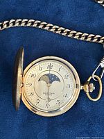 Open hunter case showing dial, moon phase, date window, and portion of chain