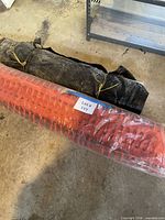 Roll of orange construction safety fence and black-wrapped bundle of wooden stakes on concrete floor
