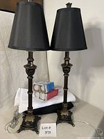 Two black and gold buffet lamps, boxes of bulbs, folded white fabric on black fabric