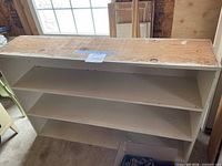 Front view of white wood shelving unit showing three shelf levels and top surface