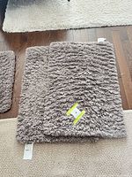 Two stacked rectangular grey shag rugs on hardwood floor, tags visible