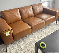 Front view of cognac leather sofa on rug with black metal legs