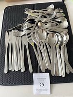 Pile of stainless steel cutlery on black mat showing knives, forks, spoons