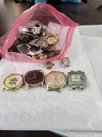 Front view of four watch cases with dials and additional parts beside open bag