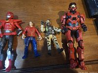 Five action figures lined up side by side on wooden surface