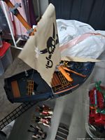 Overall view of ship hull, damaged sail, figures, cannon, treasure chest