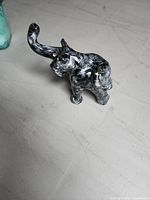 Front angle of small black ceramic elephant figurine showing trunk raised and overall paint finish