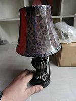 Full view of lamp showing bronze base and leopard shade wrapped in plastic