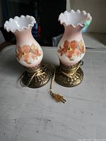 Front view showing both milk glass hurricane lamps, floral design, bases, cords
