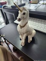 Front view of seated white unicorn figurine showing horn, necklace and body condition