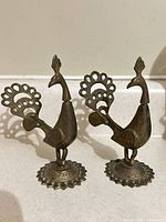 Front view of both brass peacock figurines showing overall design and patina