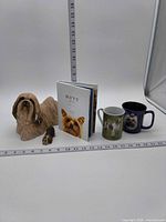 Group shot: both figurines, two mugs, book with rulers for scale