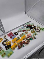 Wide view of entire assortment of earrings laid out on white backdrop with ruler for scale