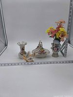 Group shot of four porcelain pieces with silk flowers and measuring tapes for scale