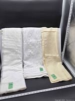 Three folded tablecloths showing colors, patterns, measurement rulers and size tags