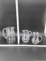 Front view of three clear glass pitchers with rulers for scale