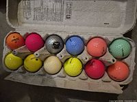 Open carton holding twelve assorted coloured golf balls