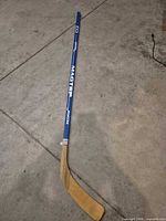 Full view of blue-shaft wooden hockey stick on floor