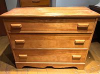 Front view of maple three-drawer Cushman chest showing pulls and scalloped base