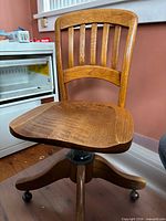 Front view showing curved slat back, oak seat, pedestal base