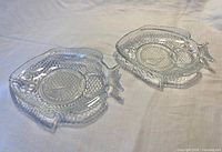 Pair of clear glass plates shaped like fish on white background