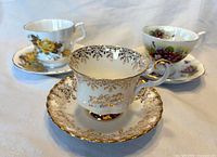 Front view of all three bone-china teacups and saucers showing patterns and gilt details