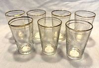Group view of seven etched wheat pattern shot glasses with gold rims
