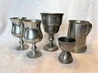 Group of five pewter drinkware items: large goblet, two medium goblets, tankard, small cup