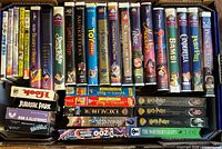 Top-down view of box showing rows of Disney clamshell VHS tapes, Harry Potter DVDs and other titles