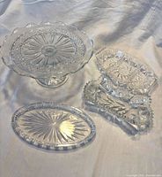 four clear glass serving pieces—pedestal cake stand, two relish dishes, octagonal tray