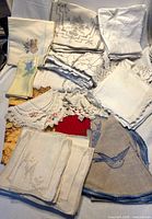 Assorted stacks of embroidered napkins, placemats, lace collars and tablecloths displayed on surface