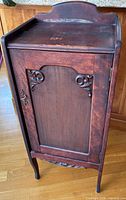 Full angled view of closed mahogany music cabinet showing door panel, carvings, legs, and gallery back