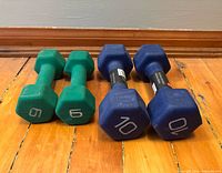 Four neoprene hex dumbbells, two green 6 lb and two blue 10 lb, displayed on wood floor