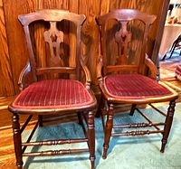 Front view of two matching Victorian Eastlake walnut dining chairs showing carved backs, arms, turned legs, and red upholstered seats