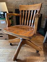 Front view of oak swivel chair with arms and slat back