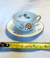 Cup on saucer with measuring tape showing dimensions and Art Deco design