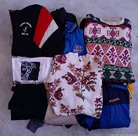 Stacked lot showing multiple sweaters, Columbia vest, Cobra Champs sweatshirt, rugby polo, graphic tee, folded dresses under layer
