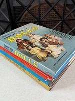 Stack of four doll reference hardcovers, spine view showing titles and authors