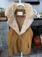 Full view of tan faux suede hooded vest on hanger