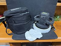 Polisher with pad installed beside carrying case and extra covers