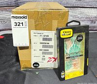 Retail-packaged OtterBox Symmetry Clear case displayed in front of unopened manufacturer carton labeled item 77-57123, carton quantity 24