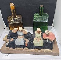 Amber and green cabin bottles positioned behind ceramic five-lady bench figurine