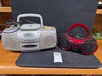 Aiwa silver CD cassette radio boombox beside GPX red/black CD radio boombox