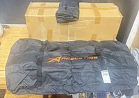 Closed shipping box with one unfolded Aceletiqs black duffel bag displaying orange logo
